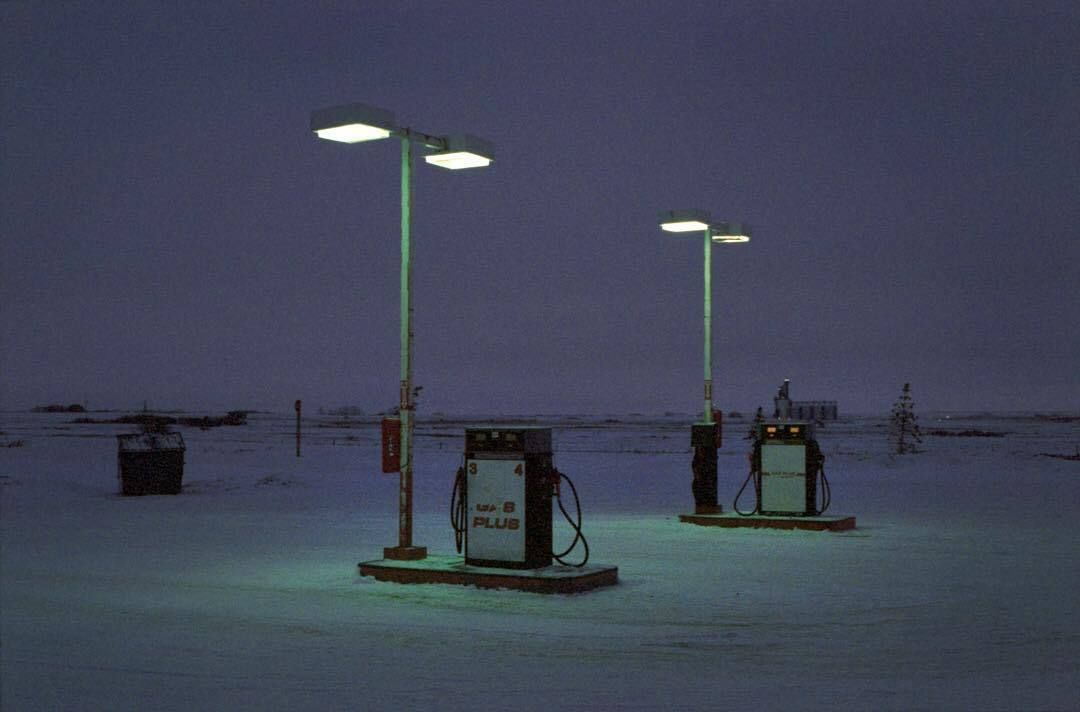 Um posto de gasolina em um cenário desértico e escuro com poucas construções